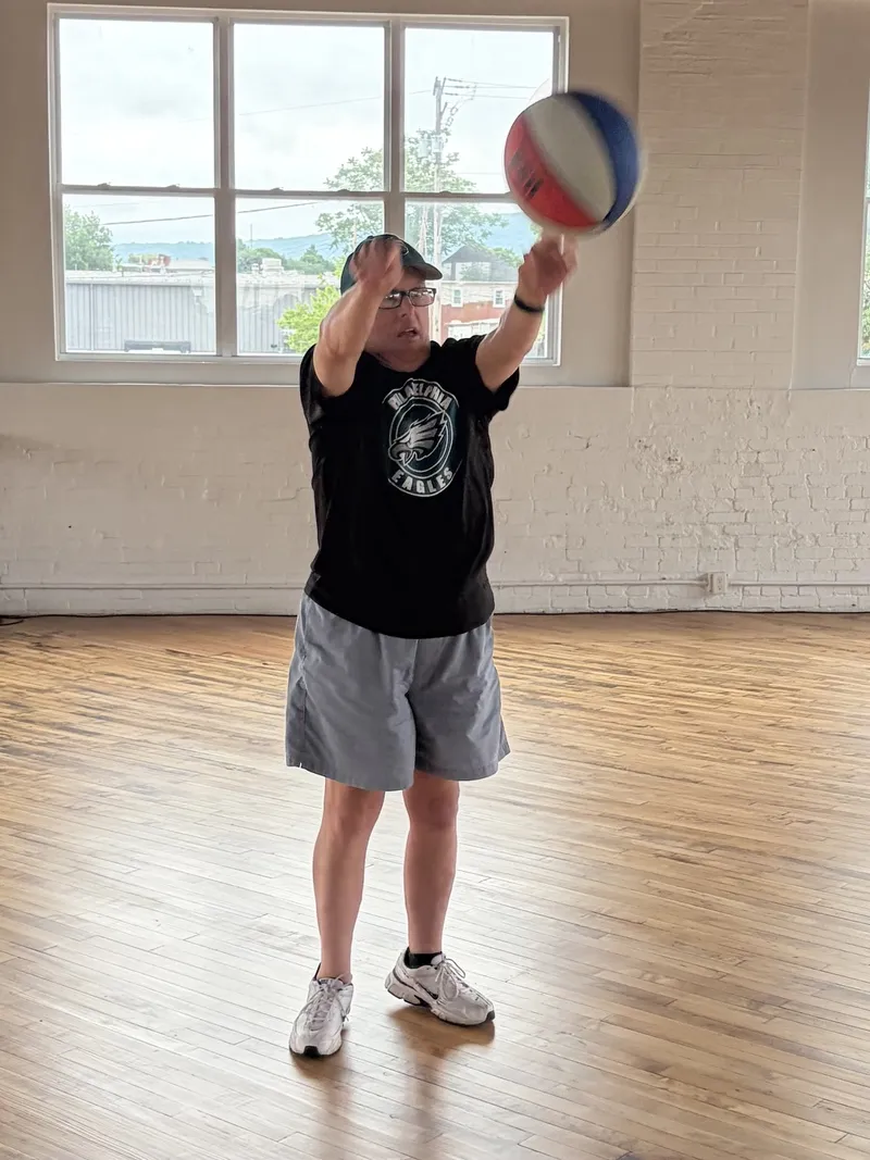 A member lines up a basketball shot in the sunlit Clubhouse gym