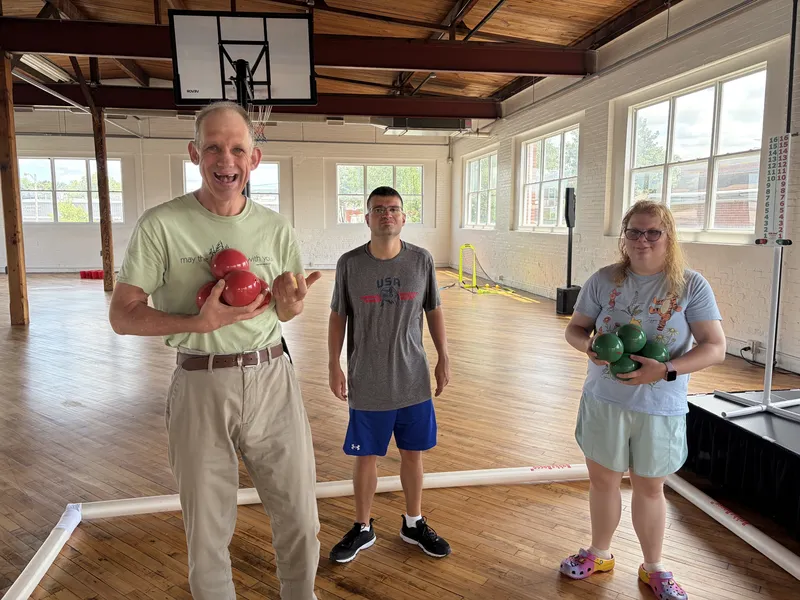 Three members hold red and green bocce balls, ready for a match